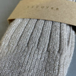 A close-up of a ribbed knit sock in a light taupe-gray color with subtle silver glitter, wrapped in a brown kraft paper band printed with the brand name ESCUYER.