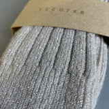 A close-up of a ribbed knit sock in a light taupe-gray color with subtle silver glitter, wrapped in a brown kraft paper band printed with the brand name ESCUYER.