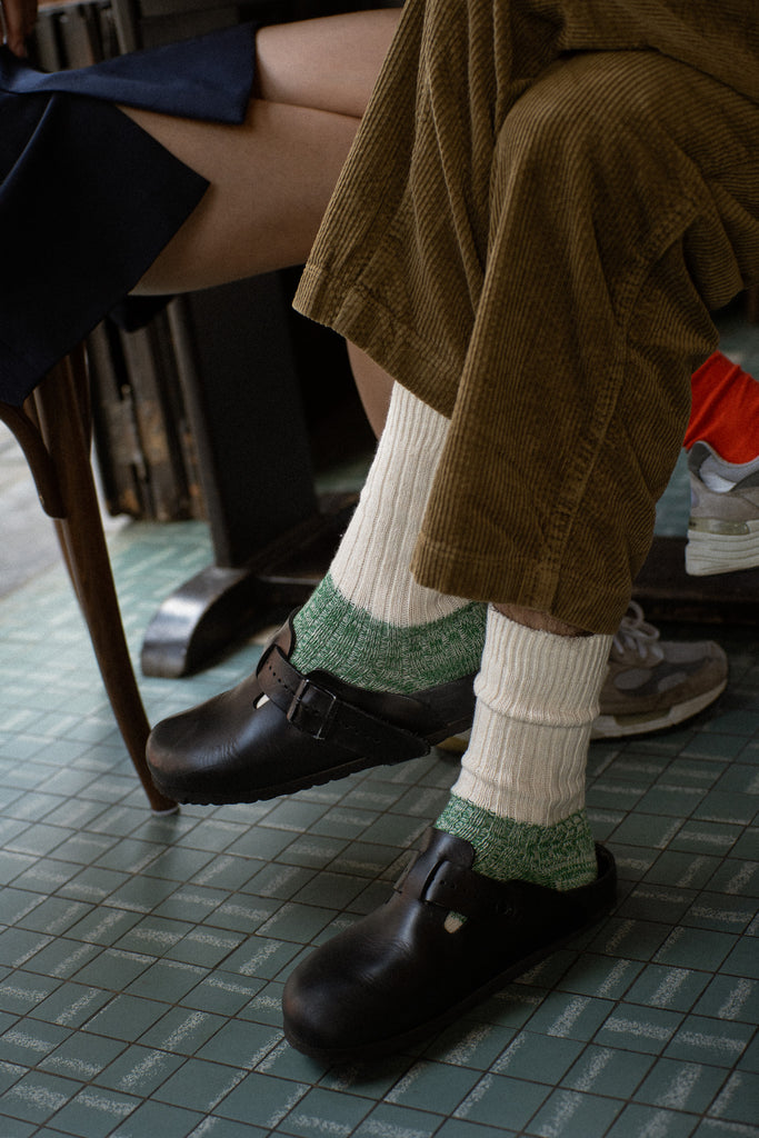 Person wearing black shoes from Birkenstock and green and white melange socks from Escuyer.