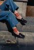 Person wearing blue jeans, black loafer shoes, and striped Escuyer socks sitting on a stone step.