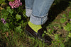 Person wearing green socks and black shoes with rolled-up jeans standing in a garden.