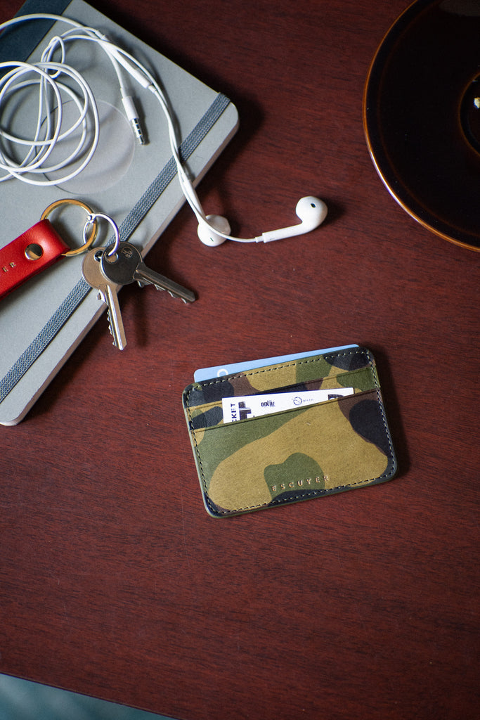 Camouflage cardholder with keys and earphones on a wooden surface