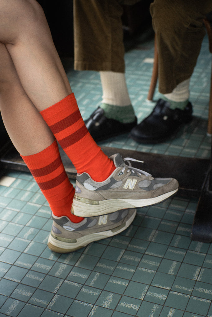 Person wearing orange striped socks and gray sneakers on a tiled floor.