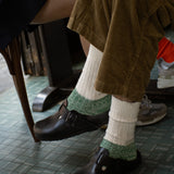 Person wearing black shoes from Birkenstock and green and white melange socks from Escuyer.