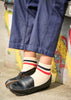 Person wearing blue shorts, black shoes, and striped socks against a colorful wall.