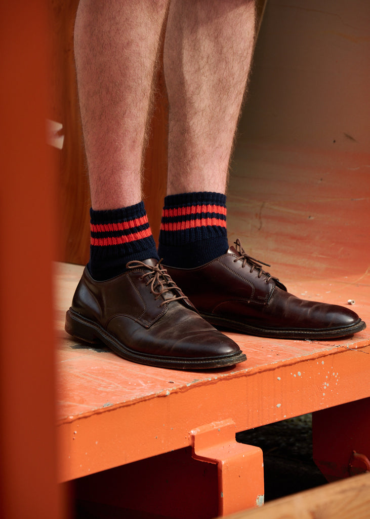 Man wearing classic brown shoes with red and navy striped ankle socks crafted from cotton yarns made in Portugal
