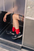 Person wearing red socks and black sneakers stepping out of a door.